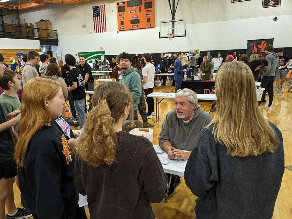 A group of people are gathered in a gym talking to a man