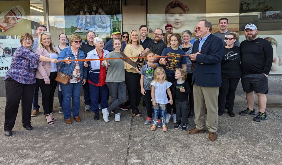 A group of people are standing in front of a building cutting a ribbon.