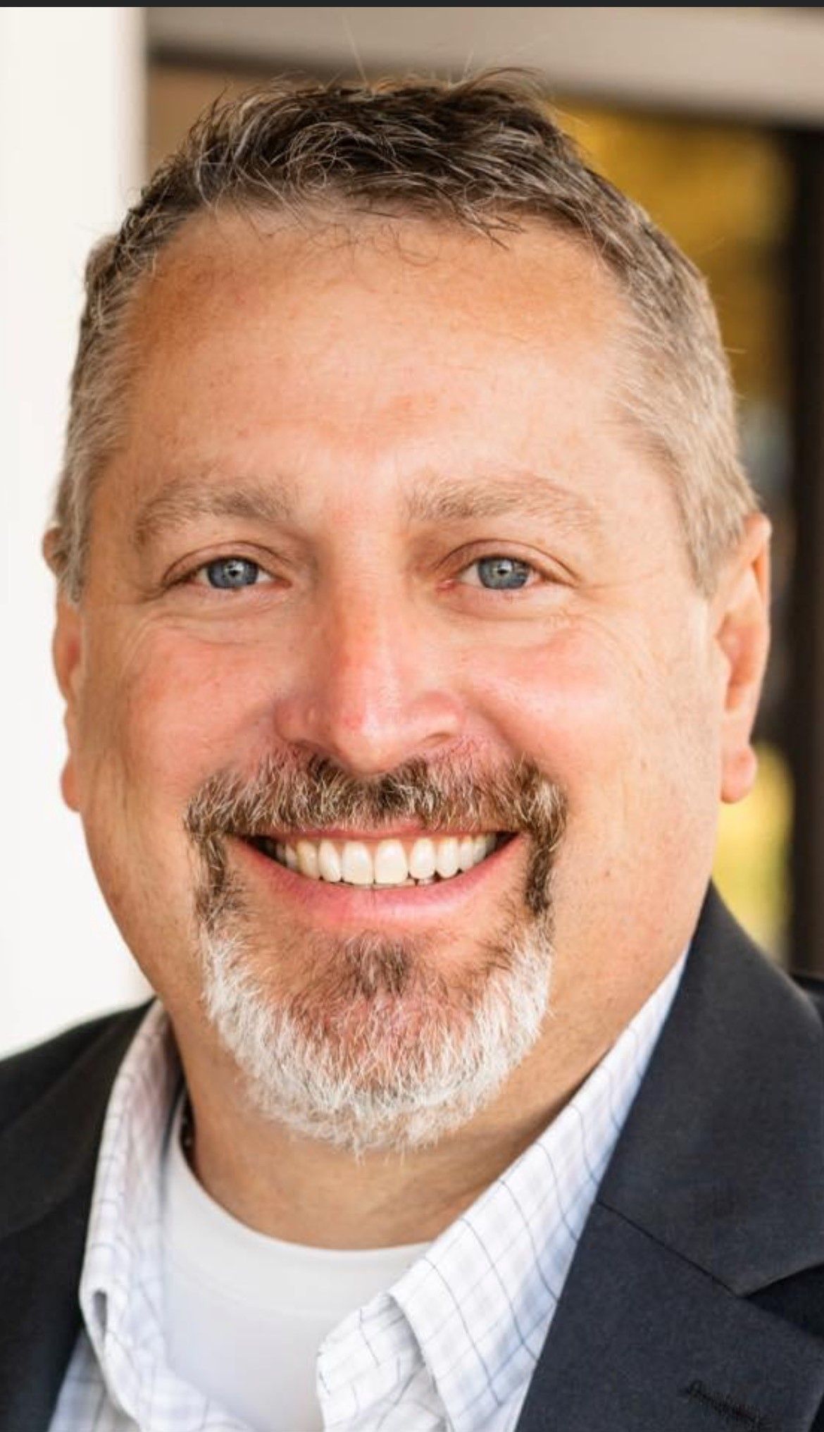 A man with a beard and a suit is smiling for the camera.