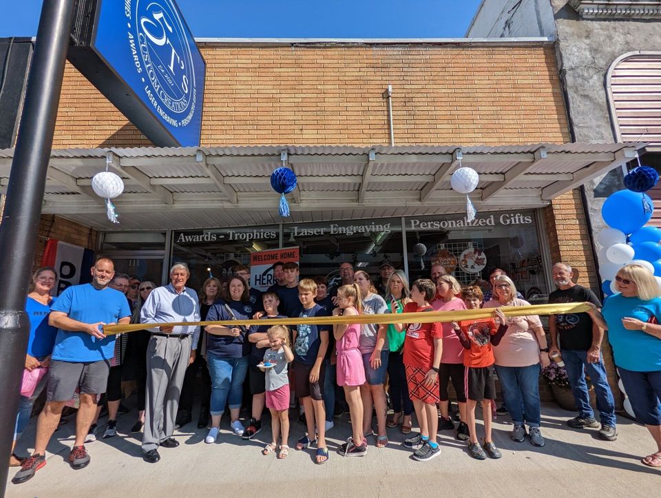 A group of people are standing in front of a store cutting a yellow ribbon.