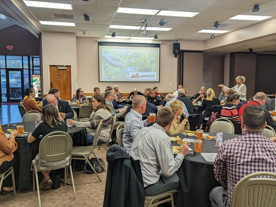 A group of people are sitting at tables in a room with a projector screen.