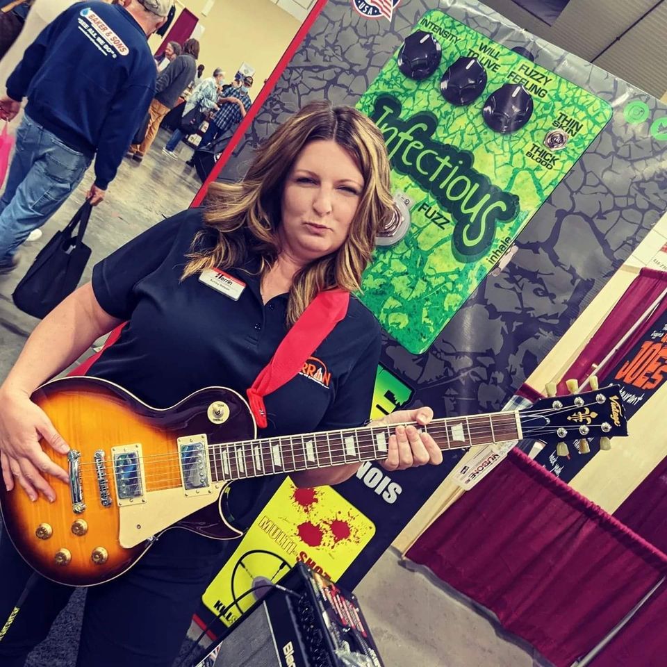 A woman holding a guitar in front of a sign that says infectious