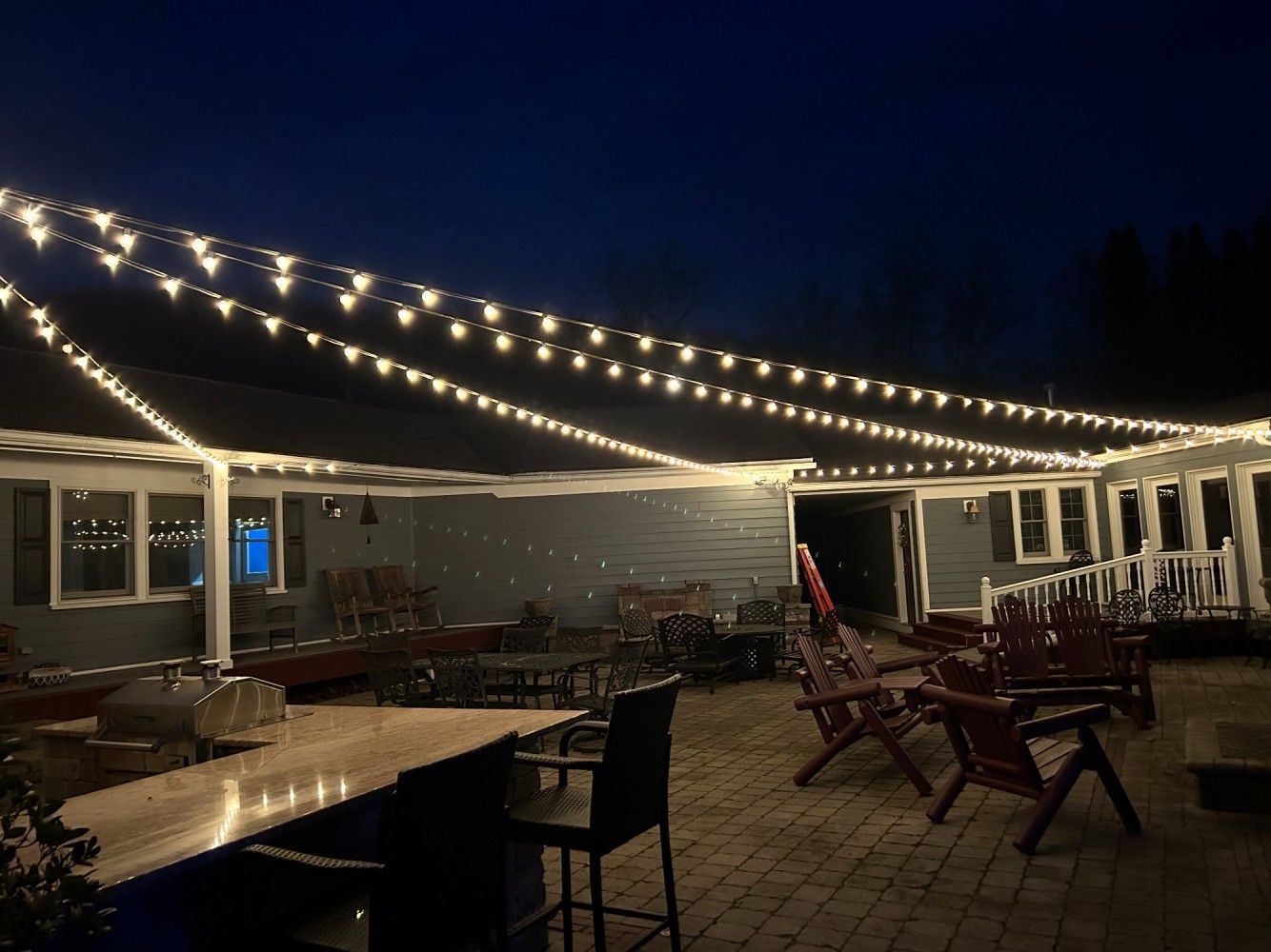 A patio with a table , chairs , and string lights at night.