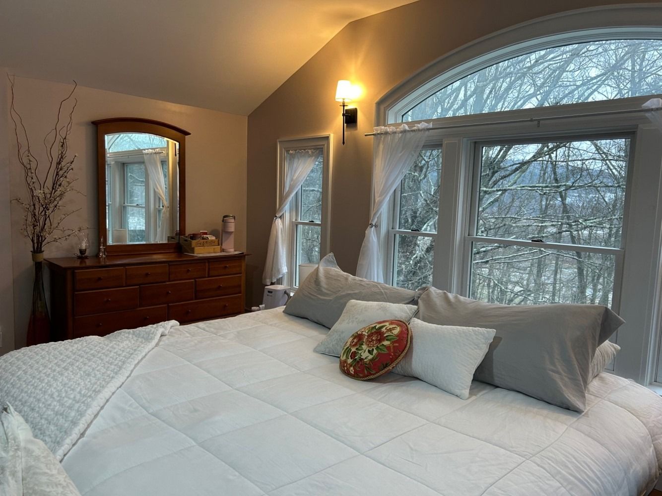 A bedroom with a large bed , dresser , mirror and window.