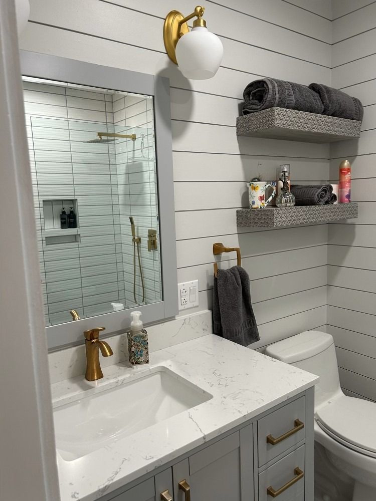 A bathroom with a sink , toilet , mirror and shelves.