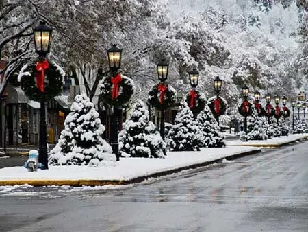 A row of street lights and christmas trees covered in snow.