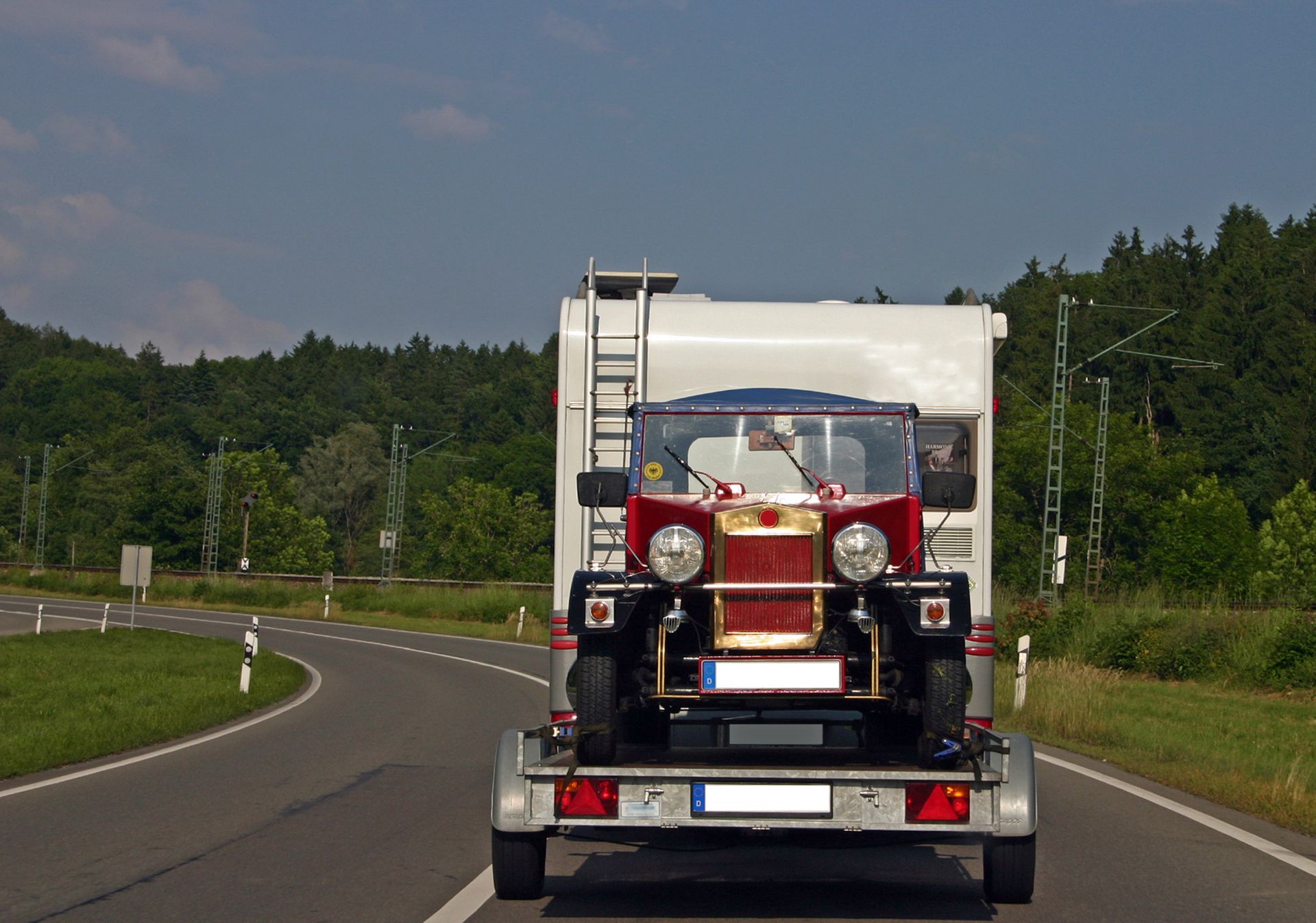 A red car is being towed by a trailer on a road