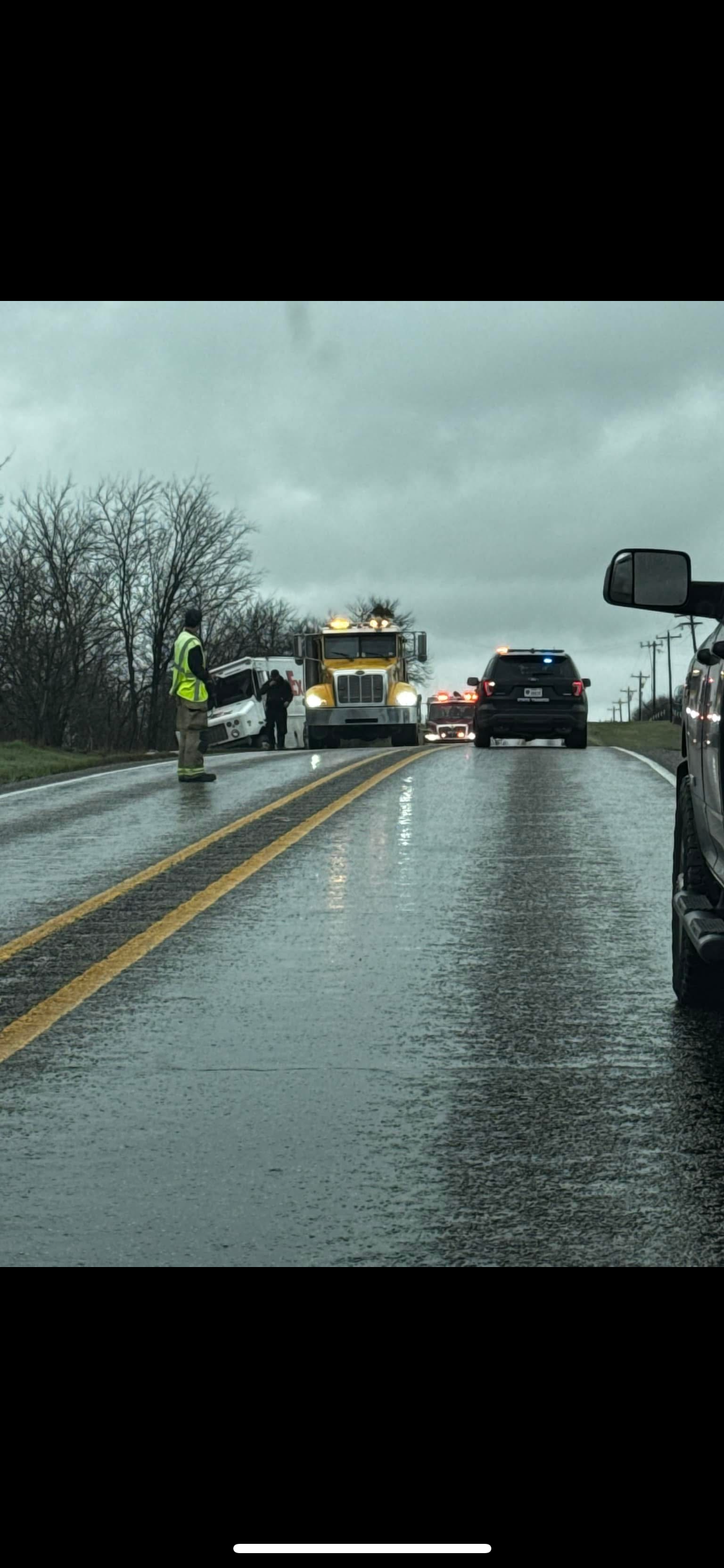 A tow truck is driving down a wet road next to a car.