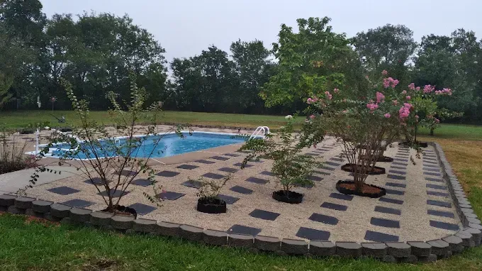 A swimming pool is surrounded by trees and a brick walkway.