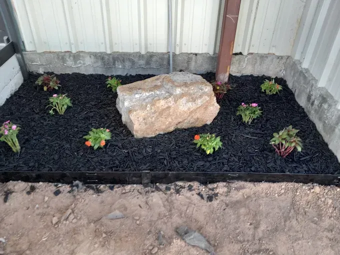 A rock is sitting in the middle of a garden surrounded by flowers.