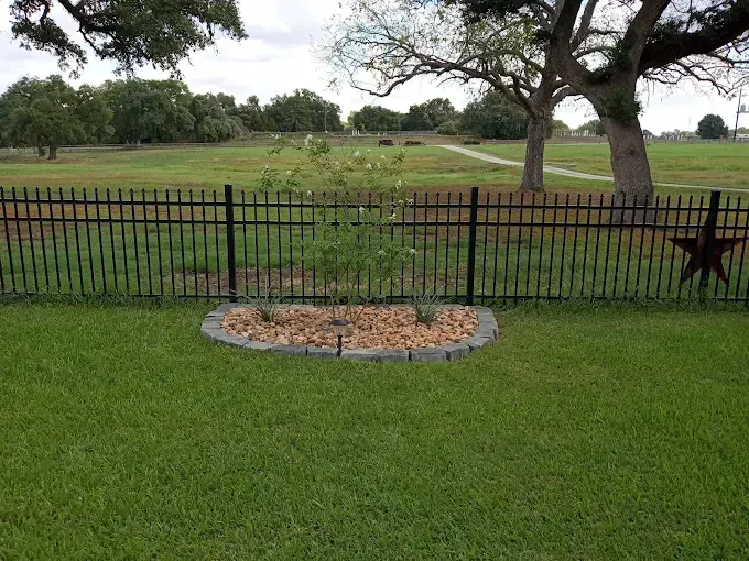 A black fence surrounds a lush green field with trees in the background.