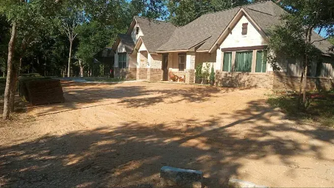 A large white house with a gravel driveway in front of it surrounded by trees.