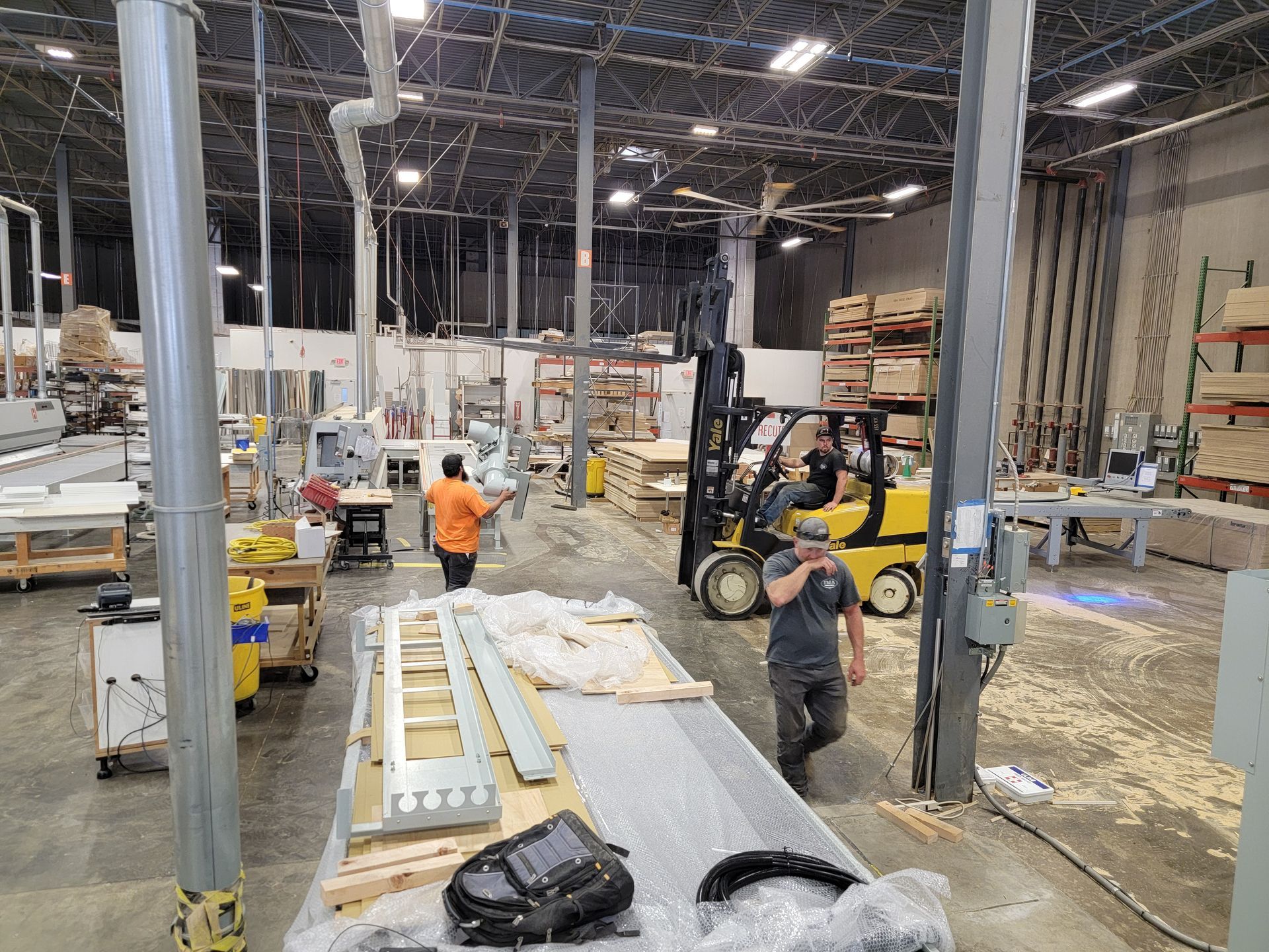 A man is walking through a warehouse with a forklift in the background.