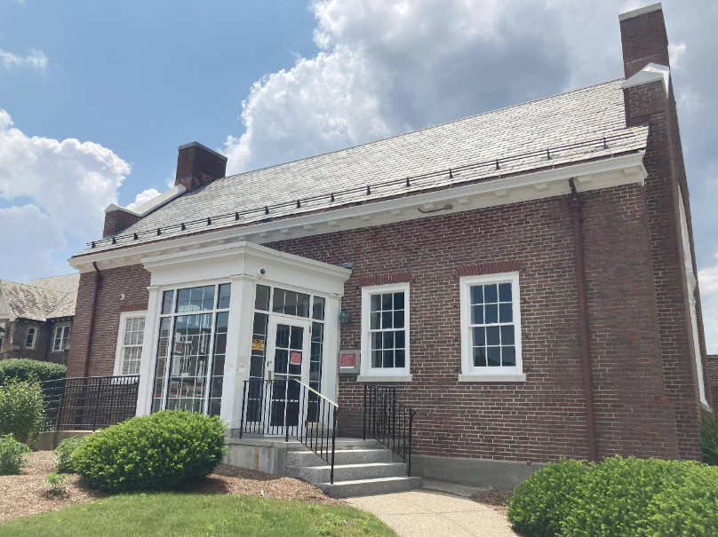 A large brick building with a white porch and windows on a sunny day.