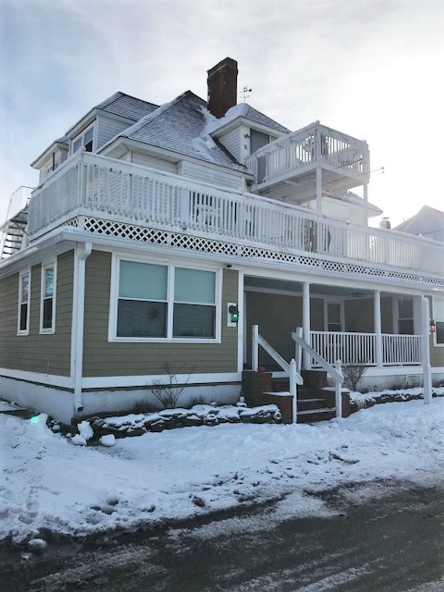 A large house with a balcony and stairs is covered in snow.