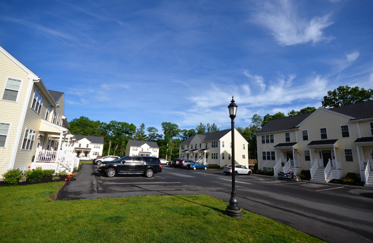 A row of houses with cars parked in front of them on a sunny day.
