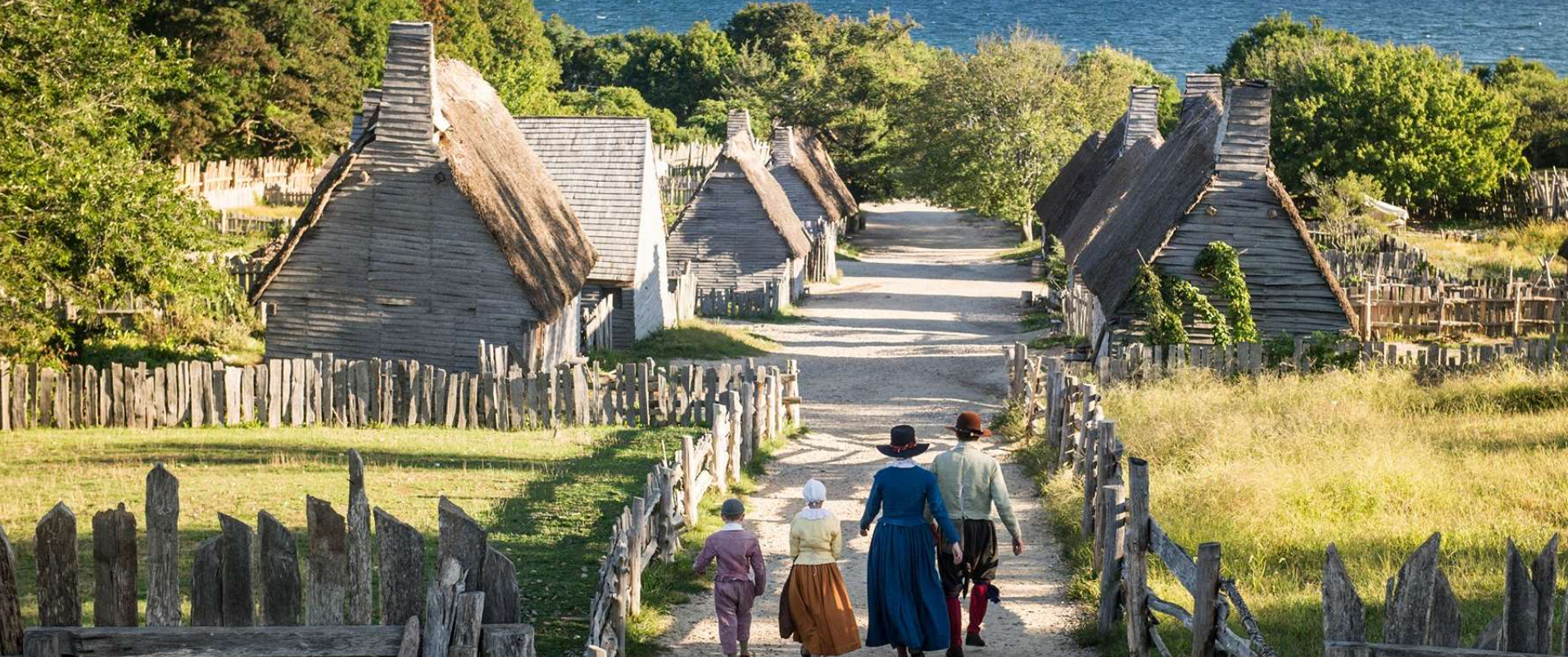 A group of people are walking down a path in front of a row of thatched houses.