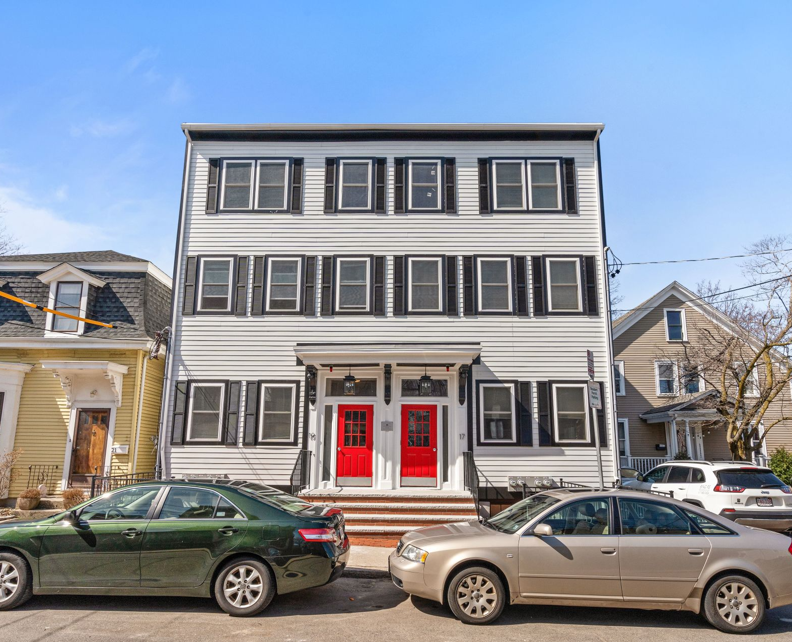 Three cars are parked in front of a building with red doors.
