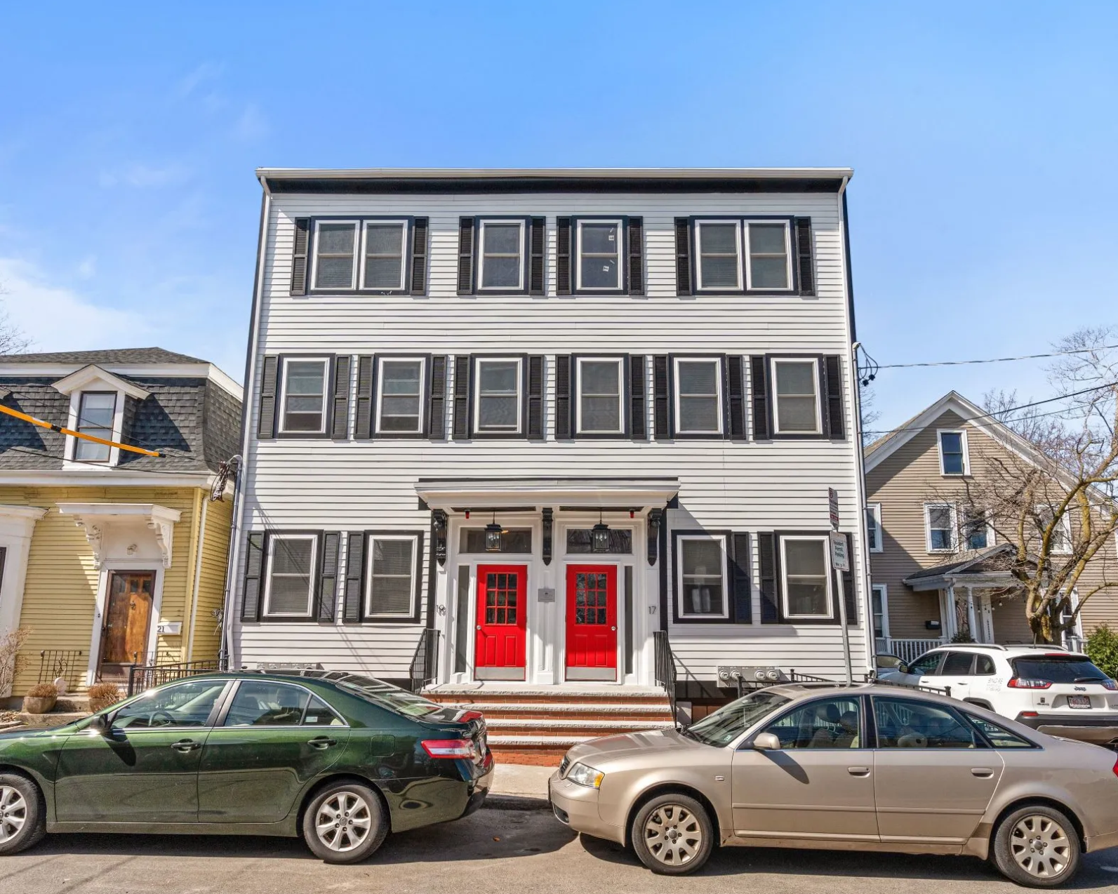 Three cars are parked in front of a building with red doors.