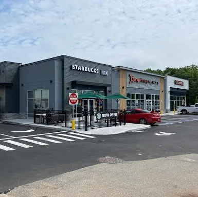 A starbucks coffee shop with a red car parked in front of it.