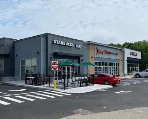 A starbucks coffee shop with a red car parked in front of it.