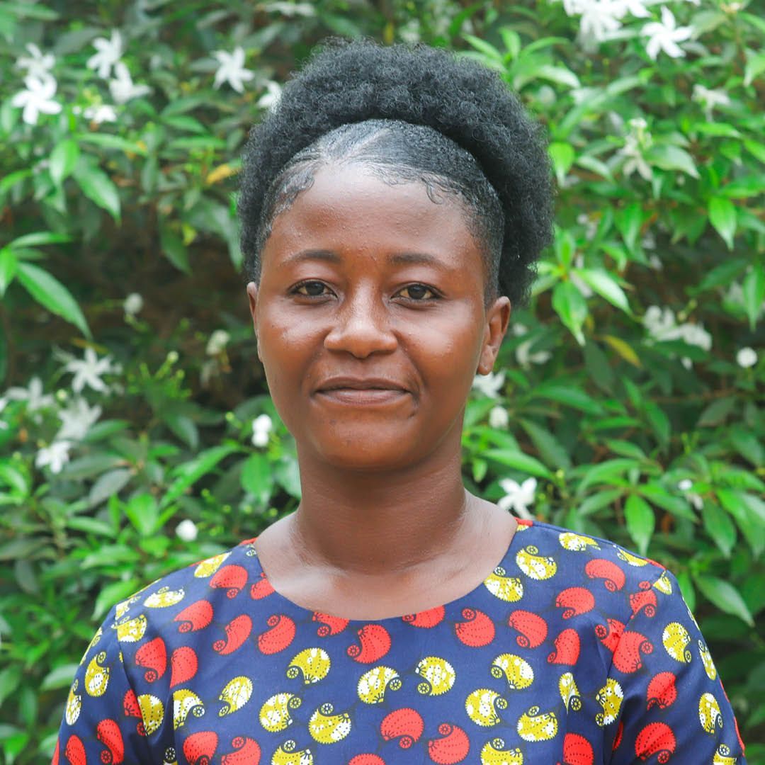 A woman in a polka dot shirt is standing in front of a bush.