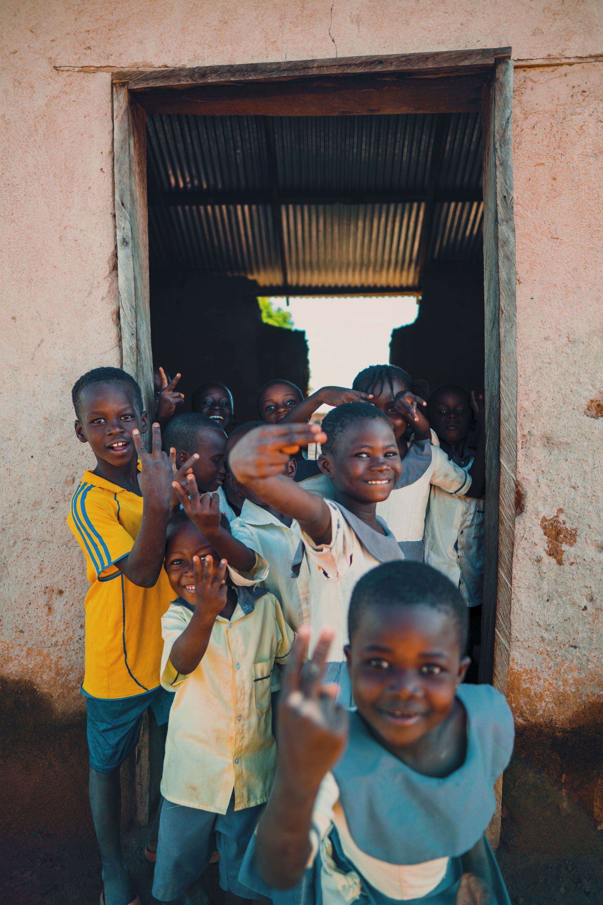 A group of children are standing in a doorway giving the peace sign.