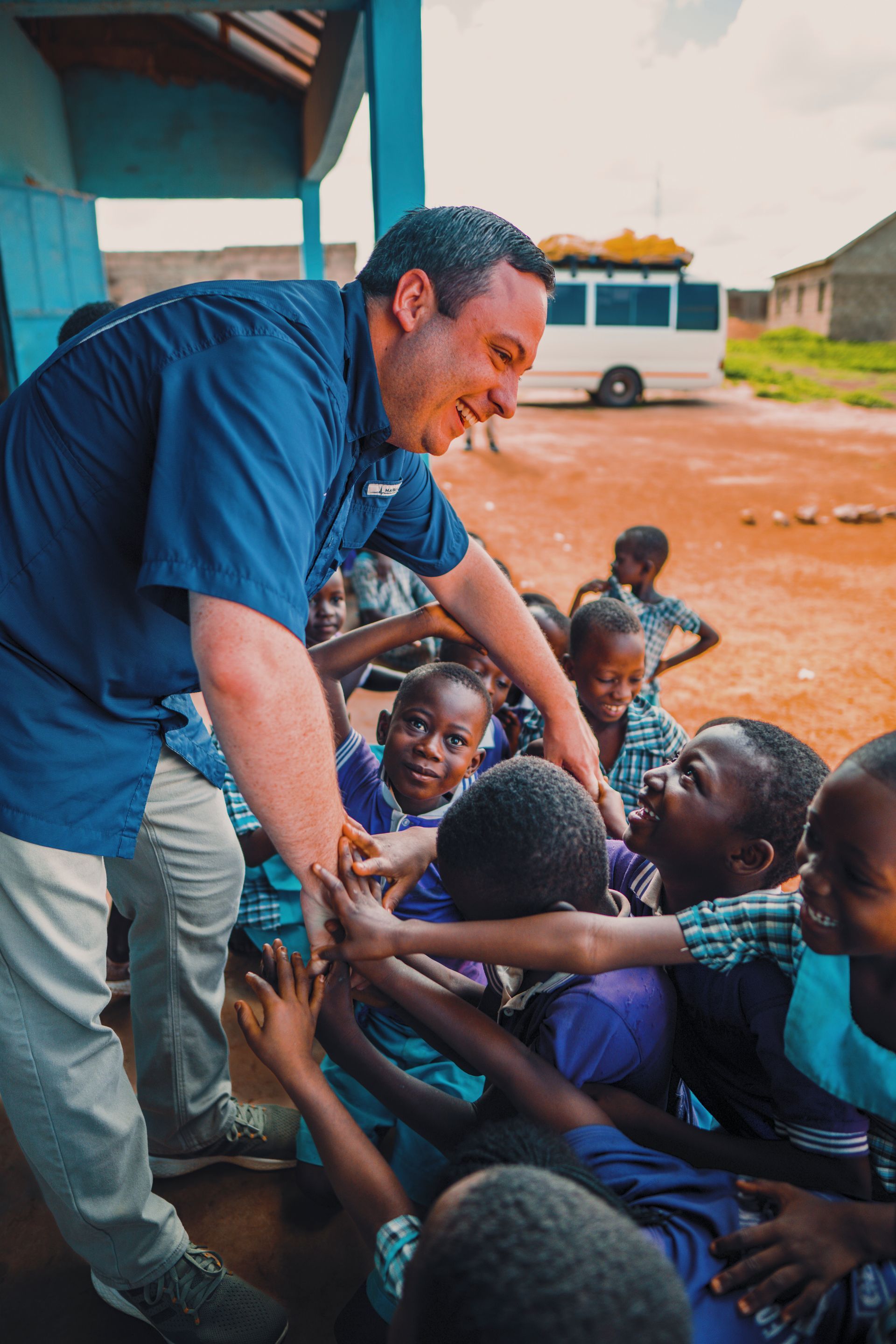 A man in a blue shirt is talking to a group of children.