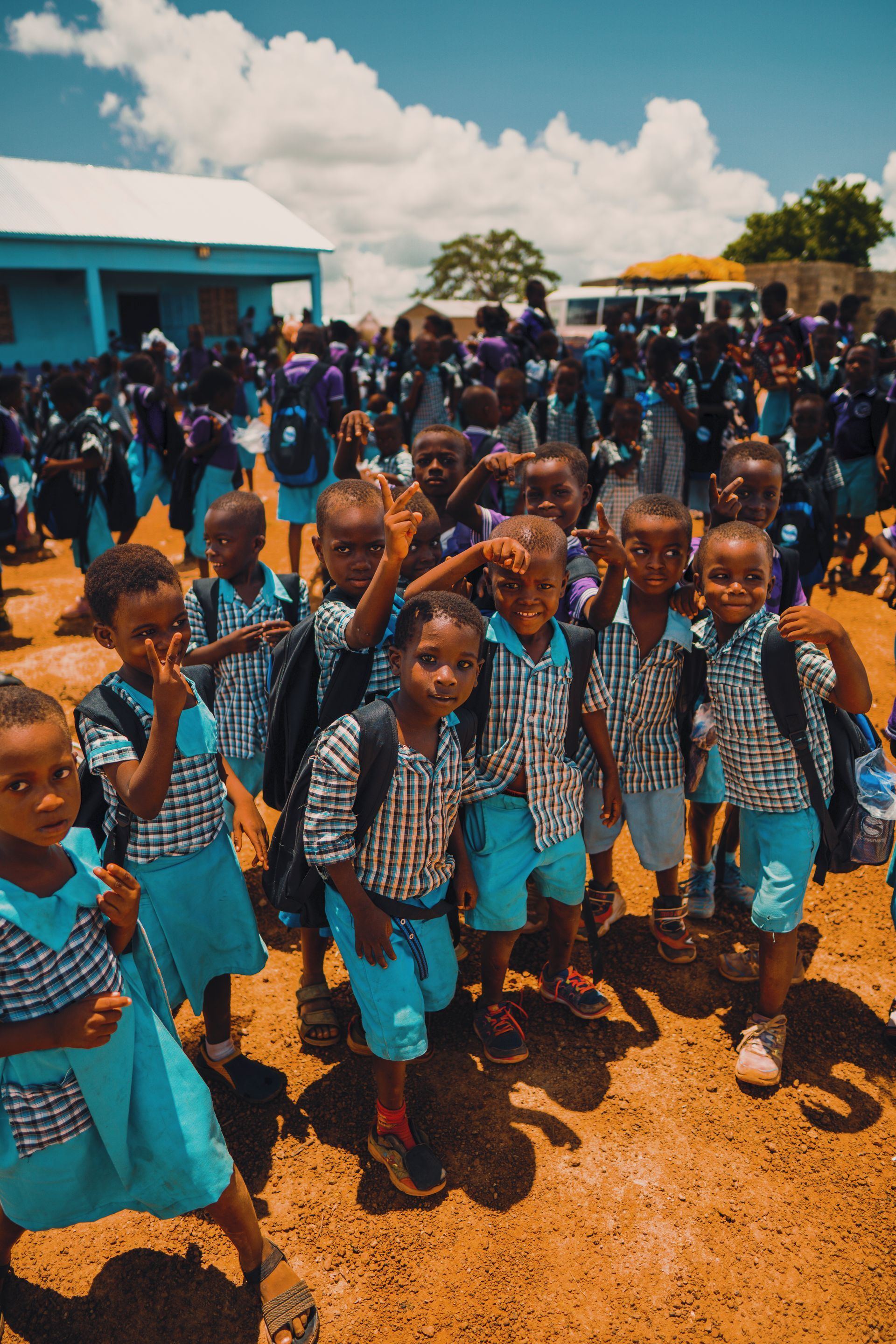 A group of children in blue uniforms are standing in a dirt field.