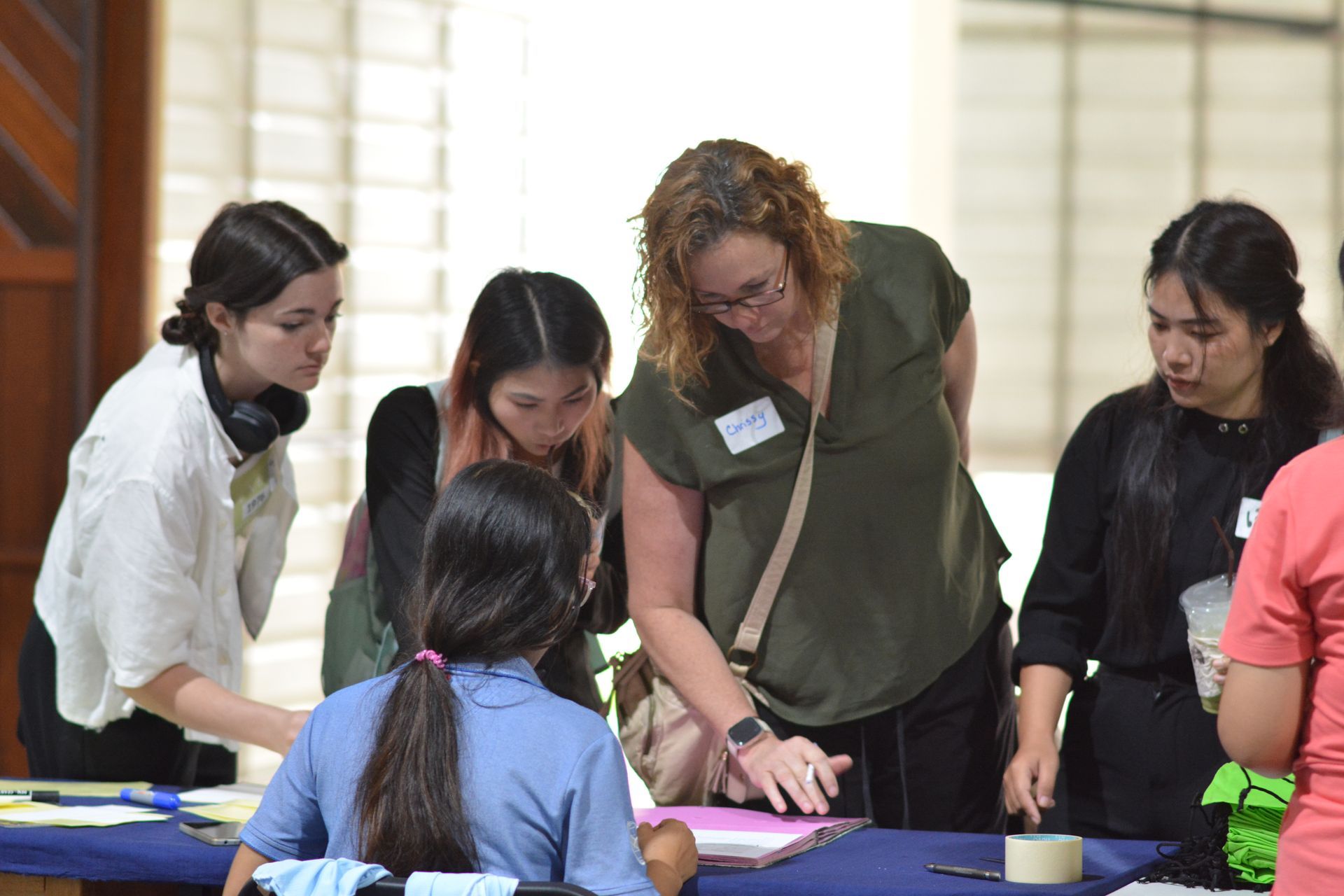 People leaning over a table, looking at papers. Some are pointing and helping a student.