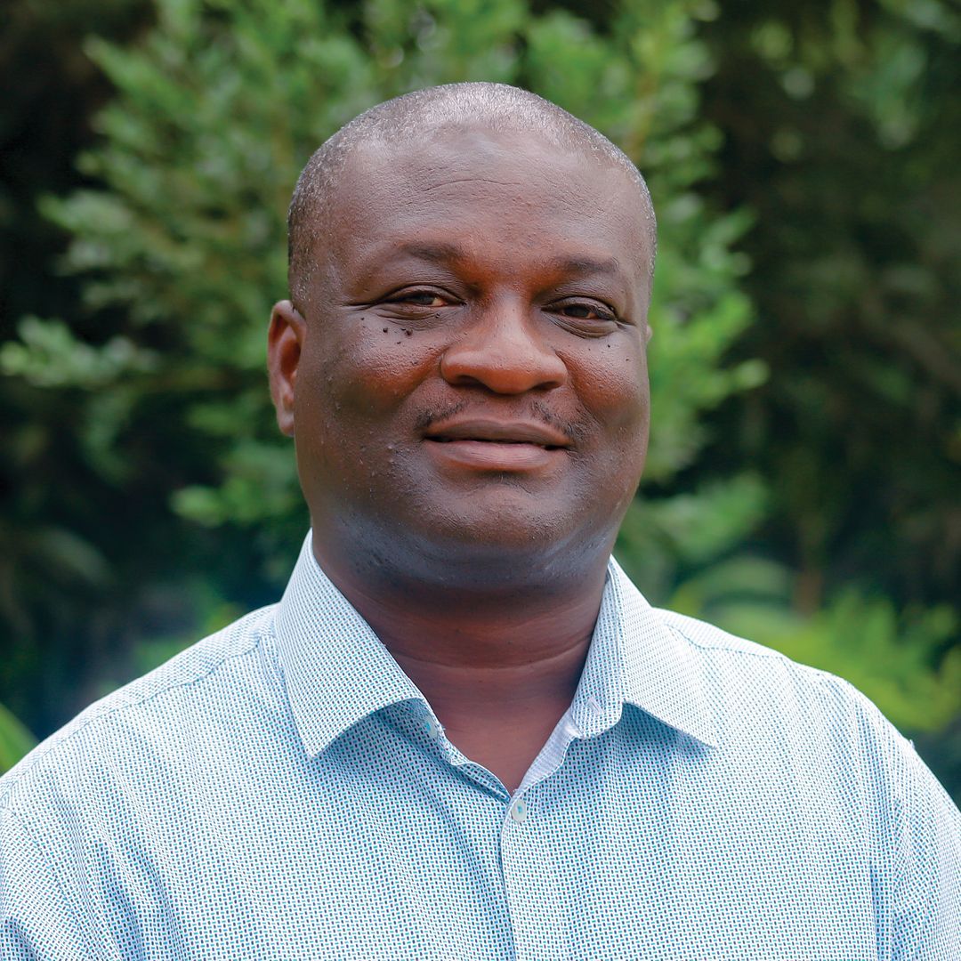 A man in a blue and purple shirt is standing in front of a tree.