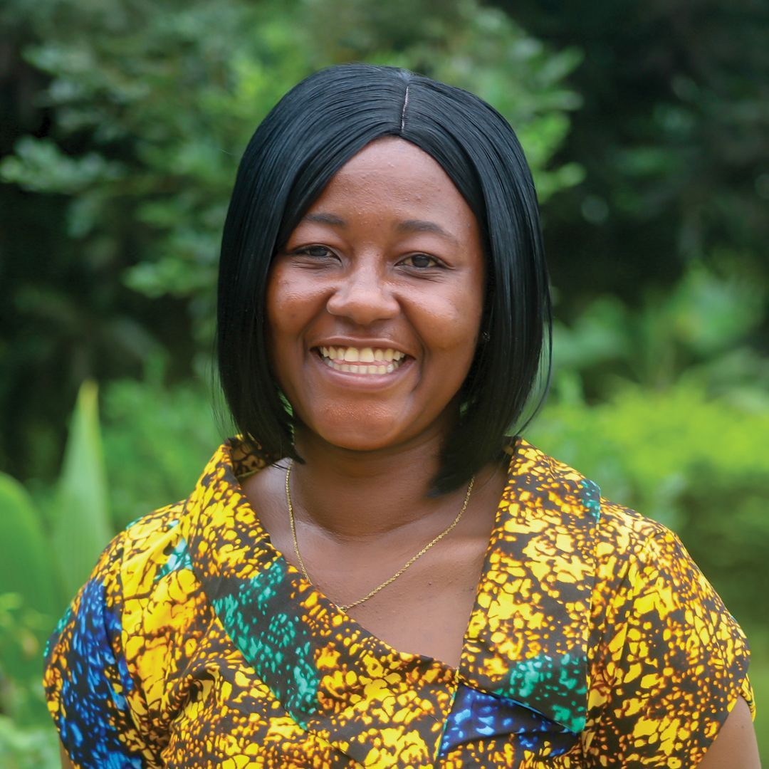A woman in a polka dot shirt is standing in front of a bush.