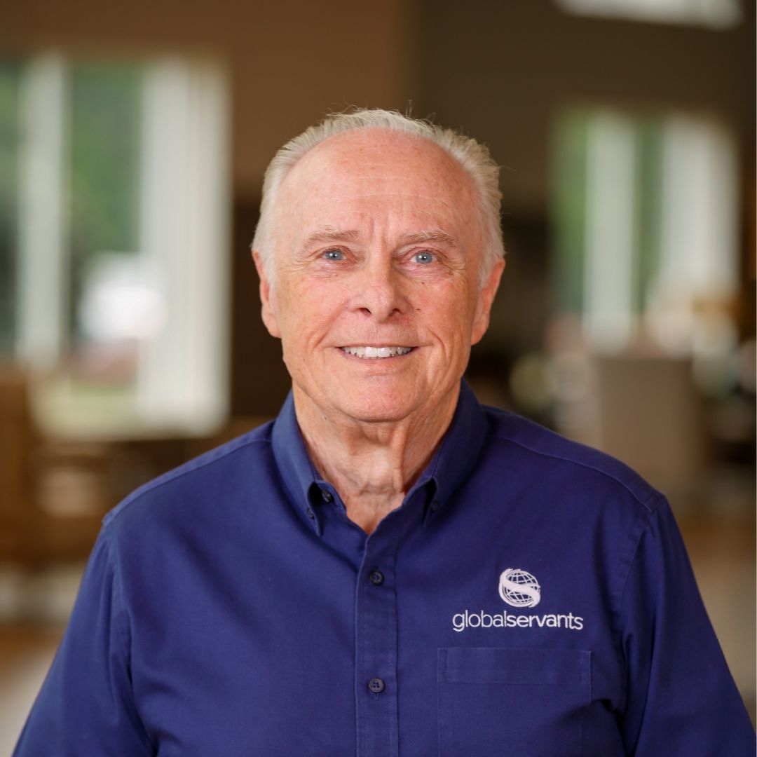 An older man wearing a blue striped shirt is smiling for the camera.