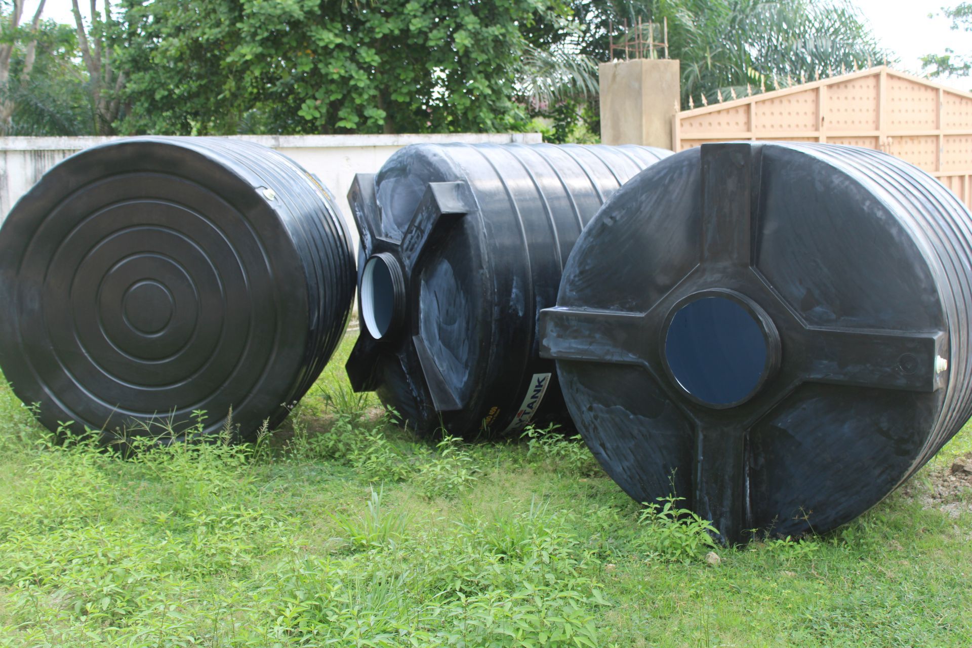 Three black plastic barrels are sitting on top of a lush green field.