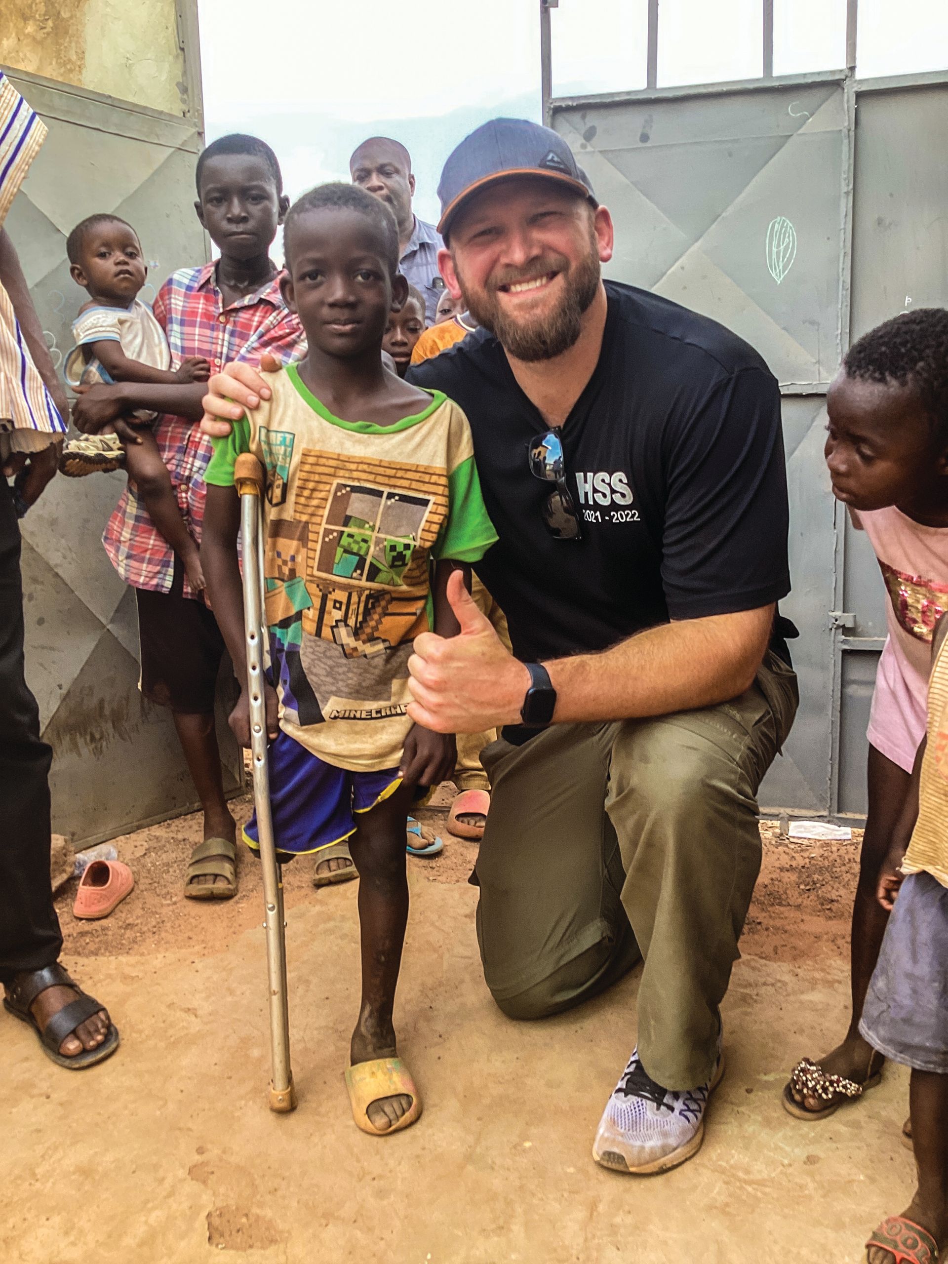 A man is kneeling down next to a young boy with a cane and giving a thumbs up.