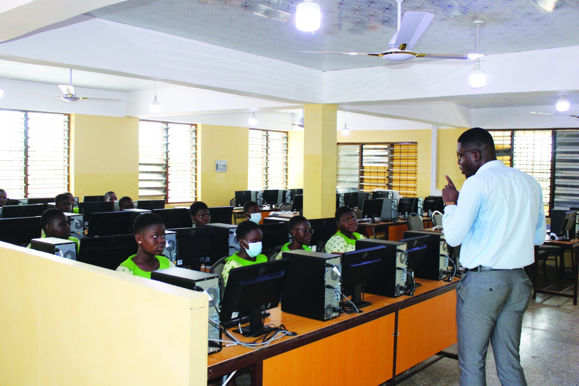 A man is standing in front of a classroom full of people using computers.