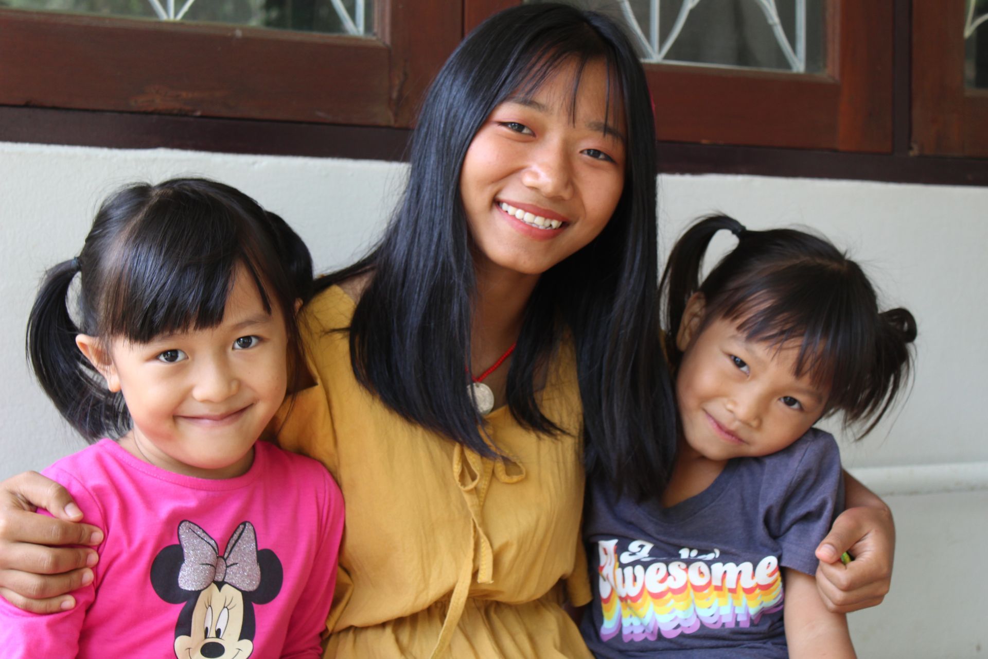 A woman and two little girls are posing for a picture . one of the girls is wearing a shirt that says awesome.