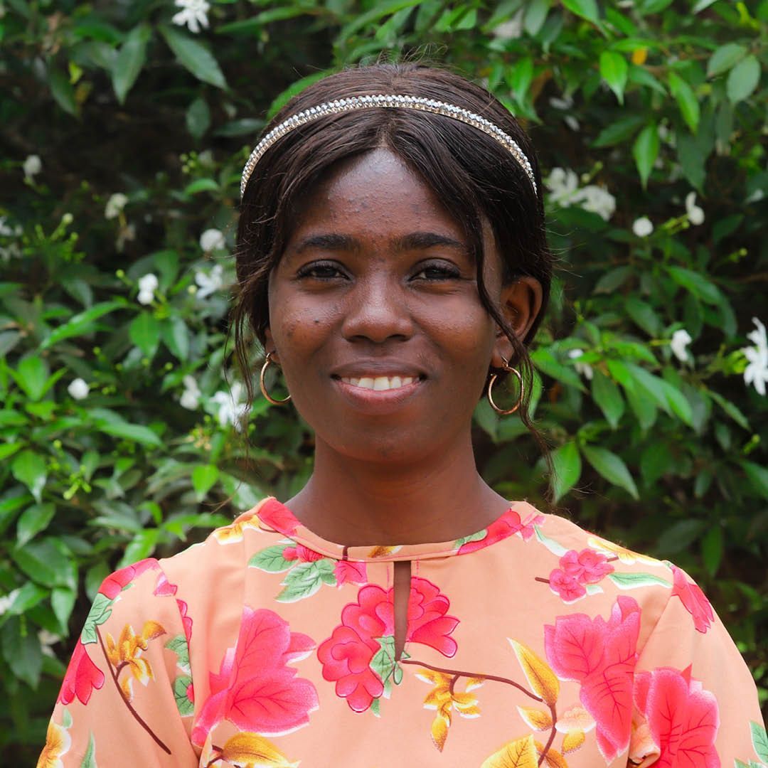 A woman in a floral shirt is smiling in front of a bush.