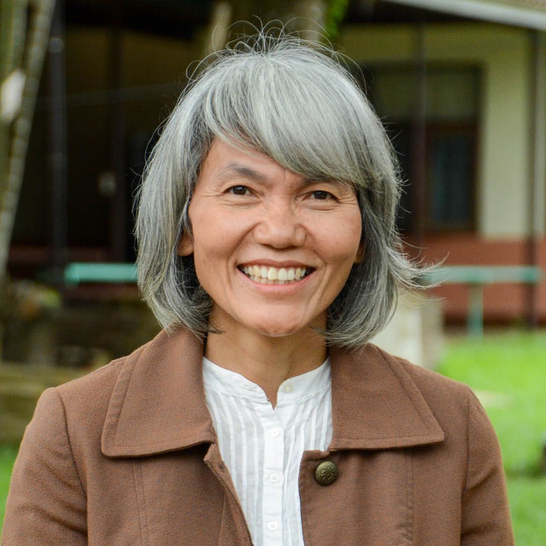 A woman with gray hair is wearing a brown jacket and smiling.