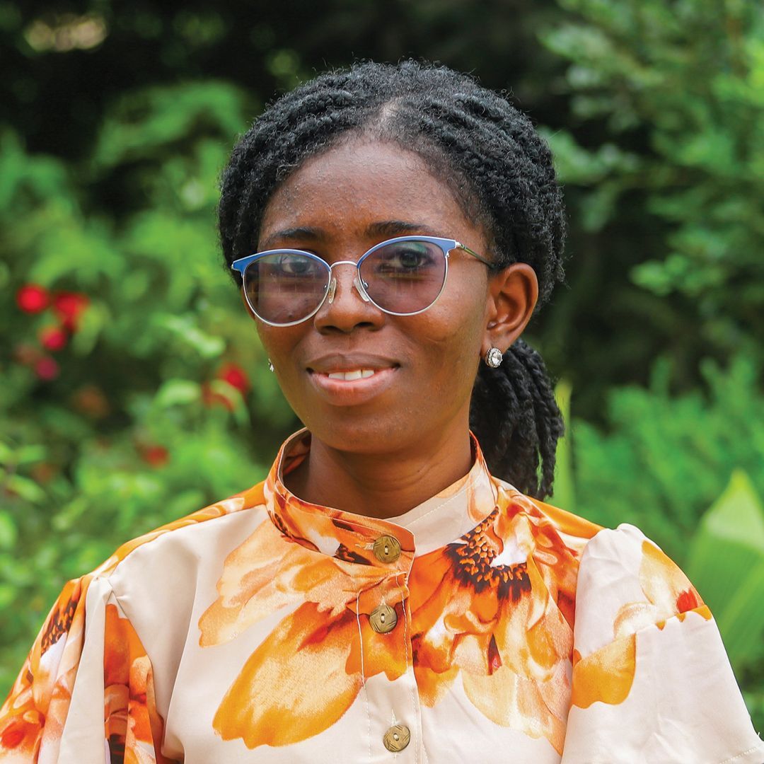 A woman in a floral shirt is smiling in front of a bush.