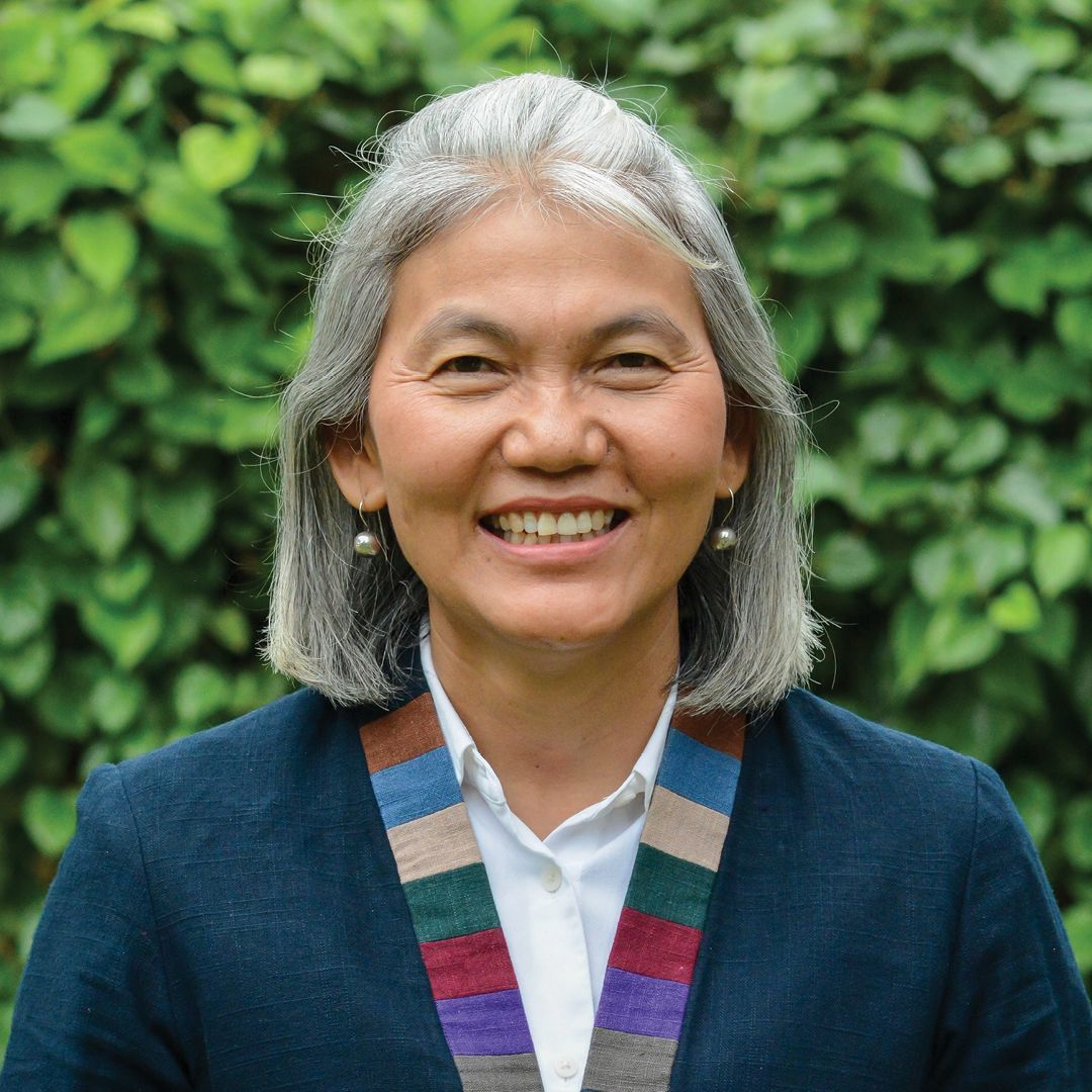 A woman with gray hair is wearing a brown jacket and smiling.