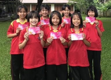 A group of young girls in red shirts are standing next to each other holding cards.