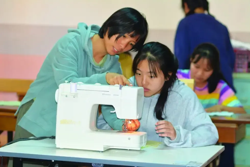 A woman is teaching a girl how to use a sewing machine