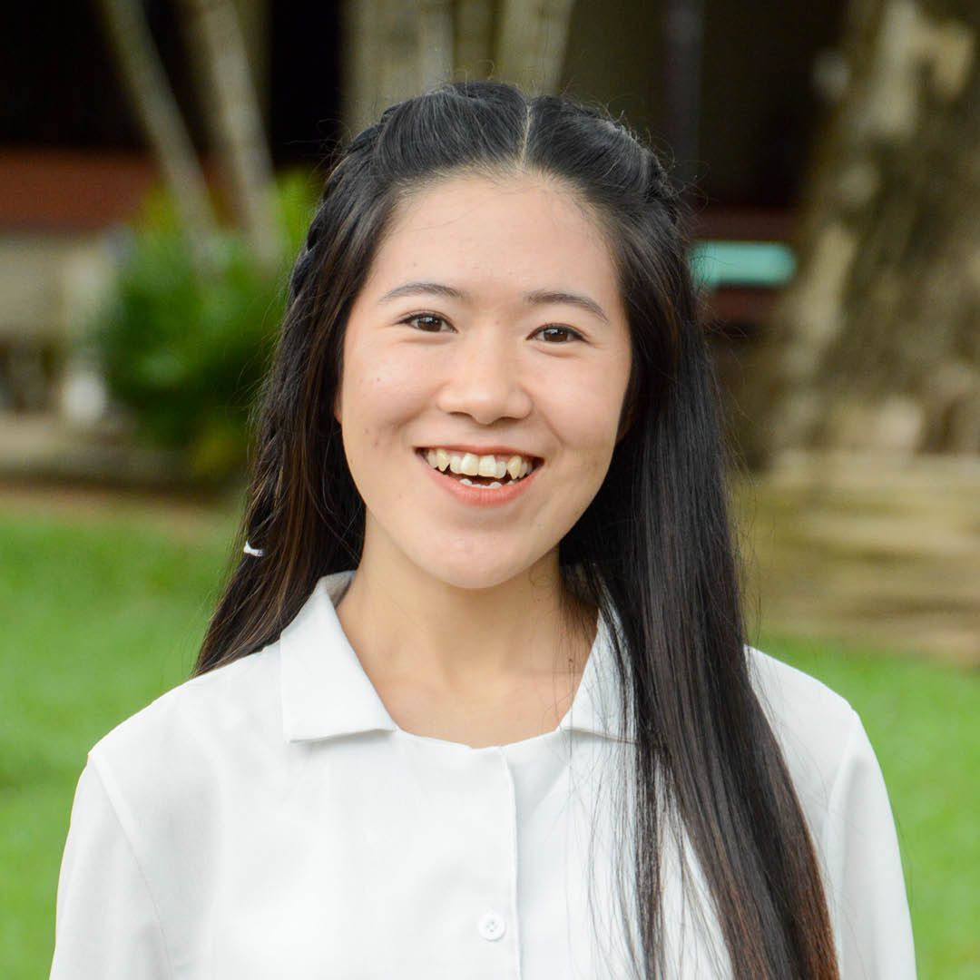 A woman with long hair is smiling and wearing a white shirt.