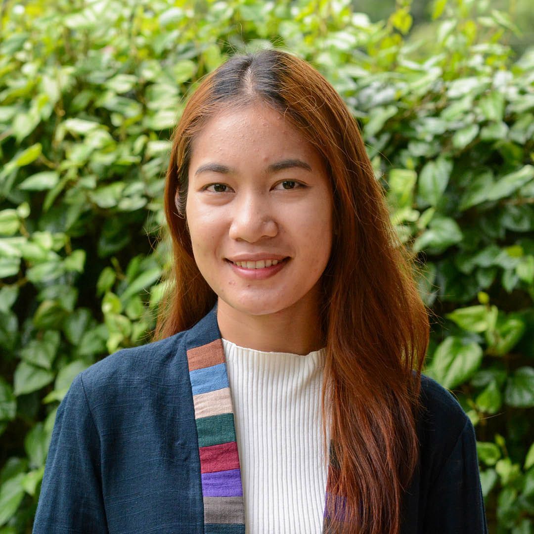 A woman is smiling for the camera in front of a bush.