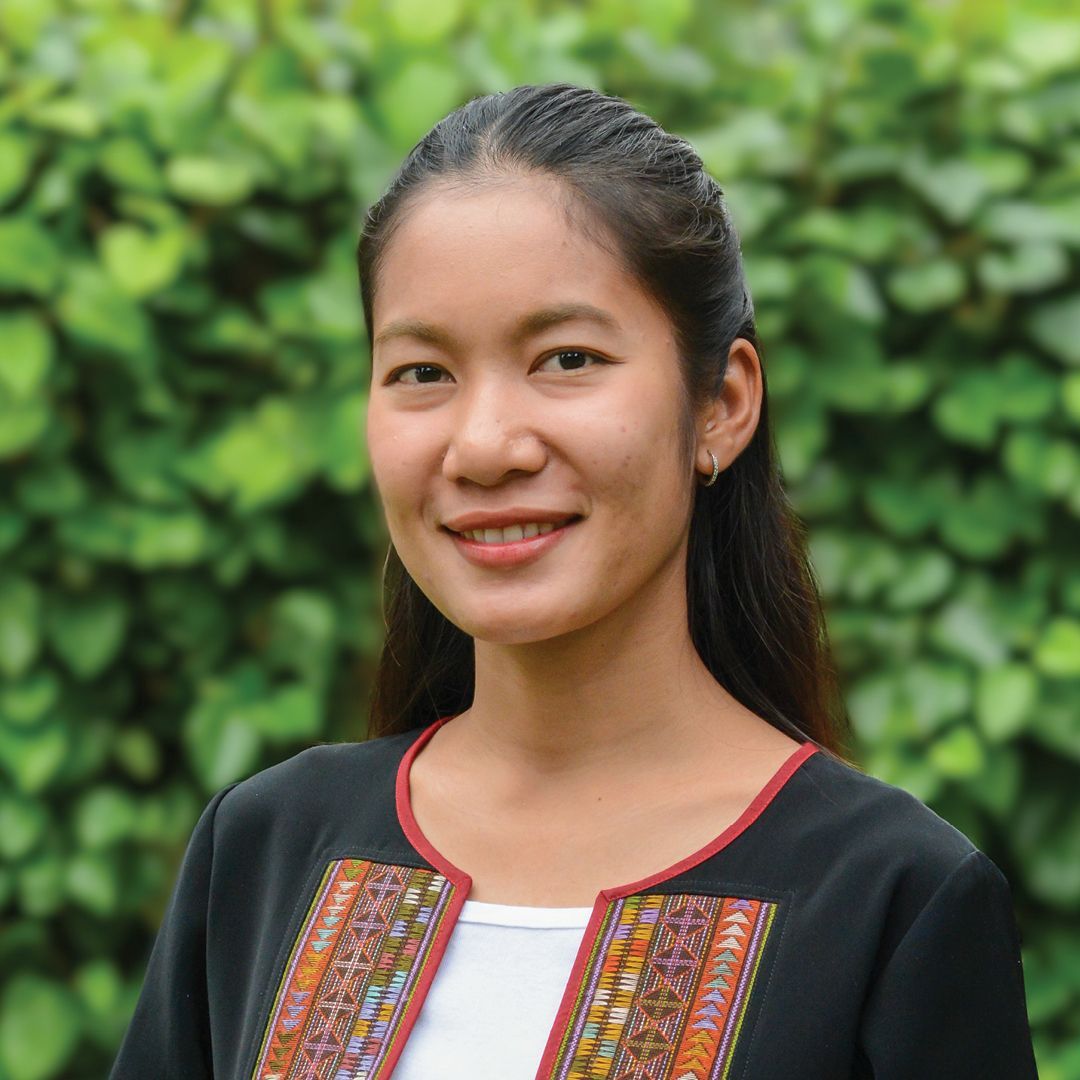 A woman is smiling for the camera in front of a bush.