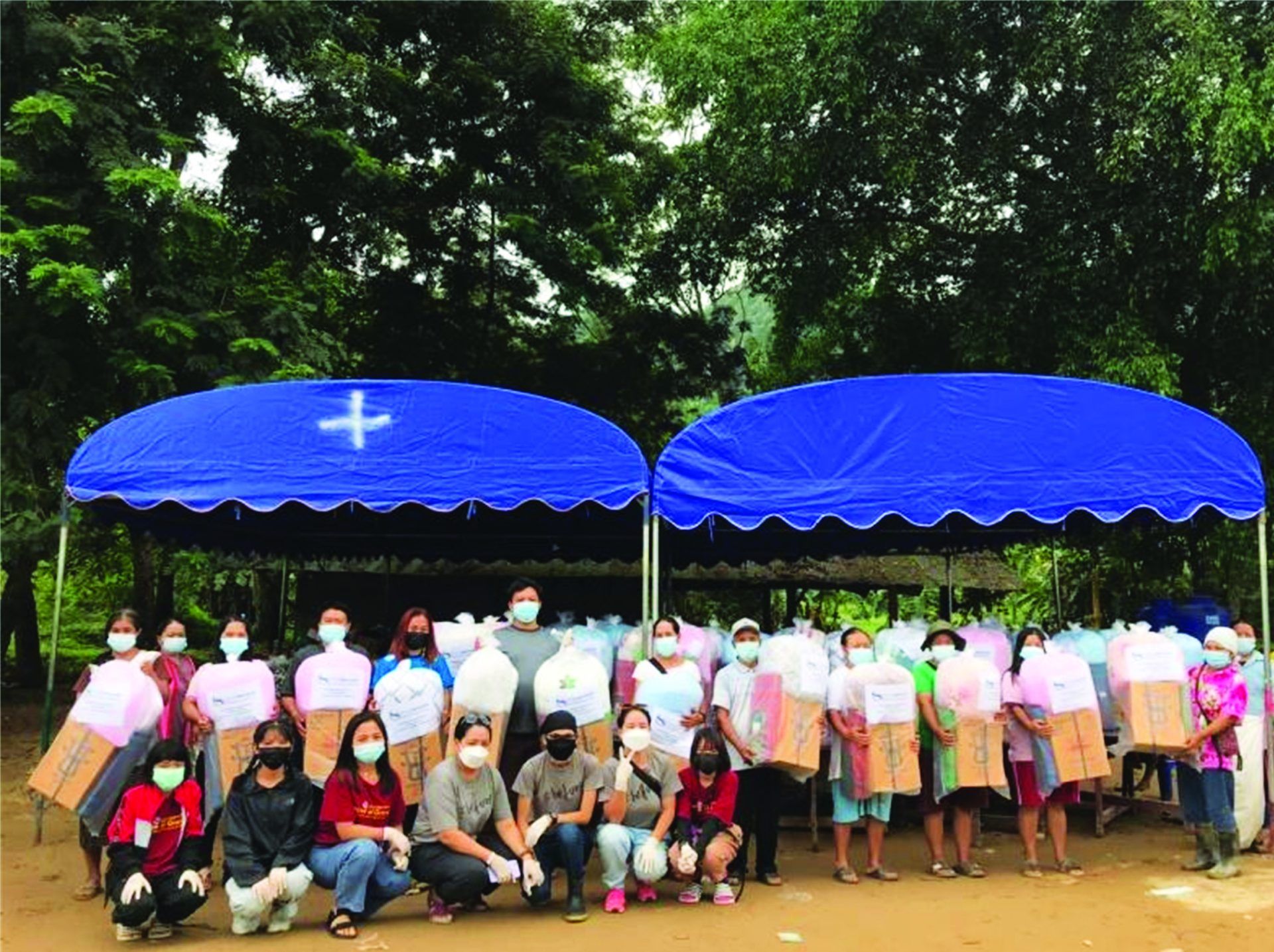 A group of people are posing for a picture under a blue tent with a cross on it