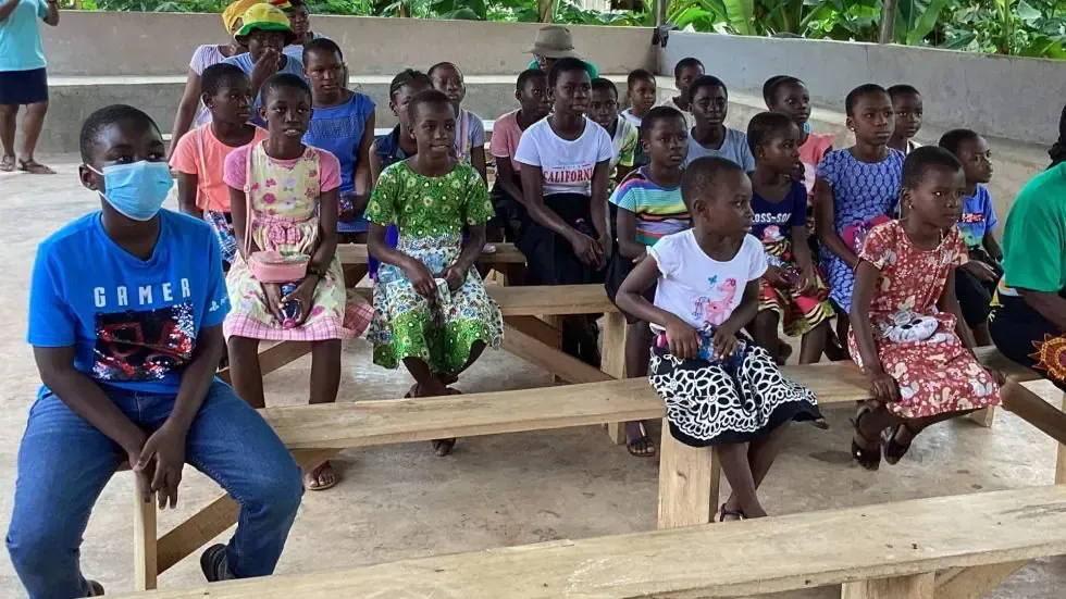 A group of children wearing face masks are sitting on wooden benches.