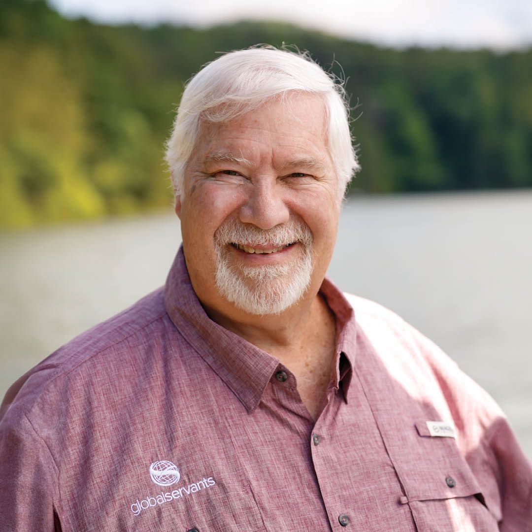 A man with a beard is wearing a purple shirt and smiling.