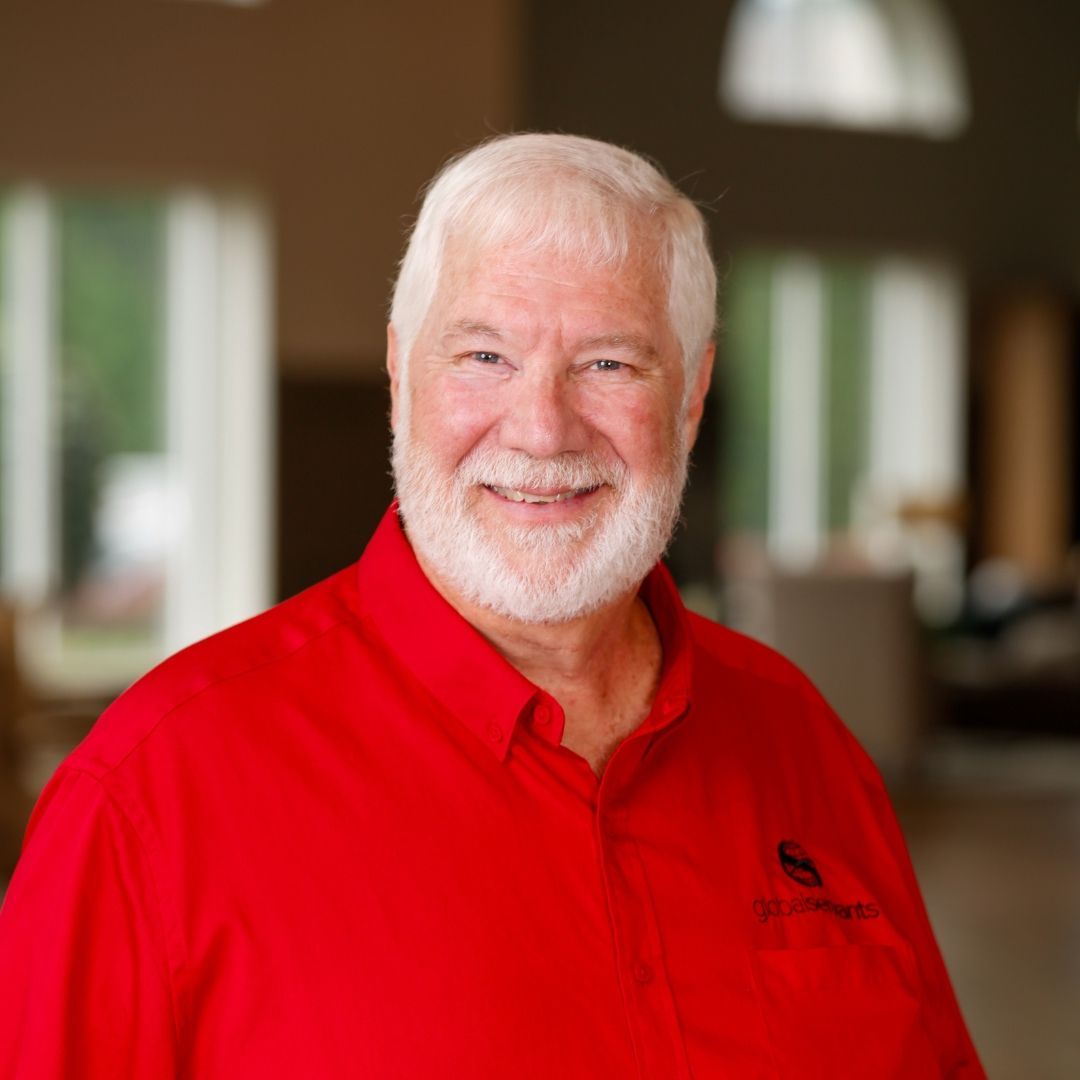 A man with a beard is wearing a purple shirt and smiling.